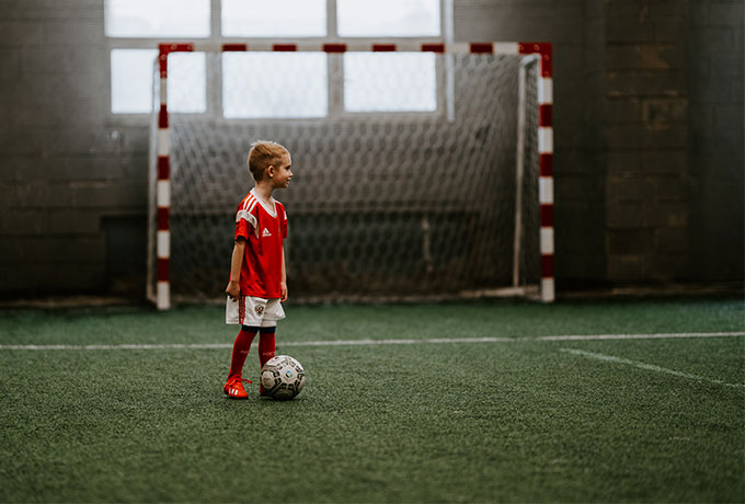 Kind mit einem Fußball in einer dunklen Sporthalle