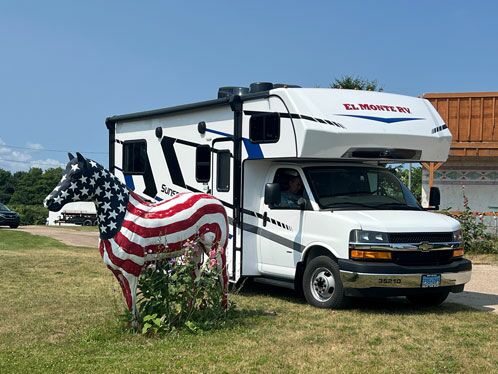 Weißes Campingmobil, davor eine Kuh aus Plastik, bemalt mit der amerikanischen Flagge