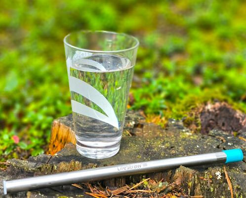 Wasserfilter LifeStraw Sip mit einem Glas Wasser auf einem Baumstumpf